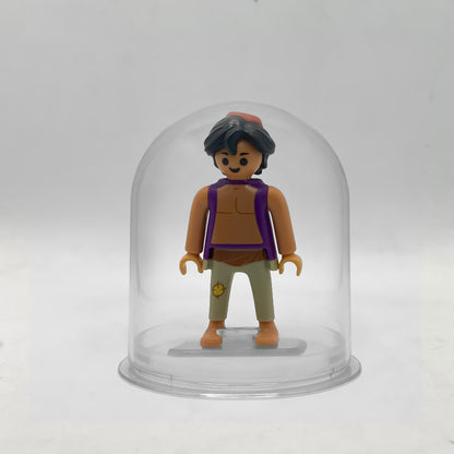 Minifigura Playmobil de Aladín con chaleco morado y fez rojo, montada sobre su peana original Playmobil dentro de la urna expositora transparente, colección Disney Kinder FCO1004