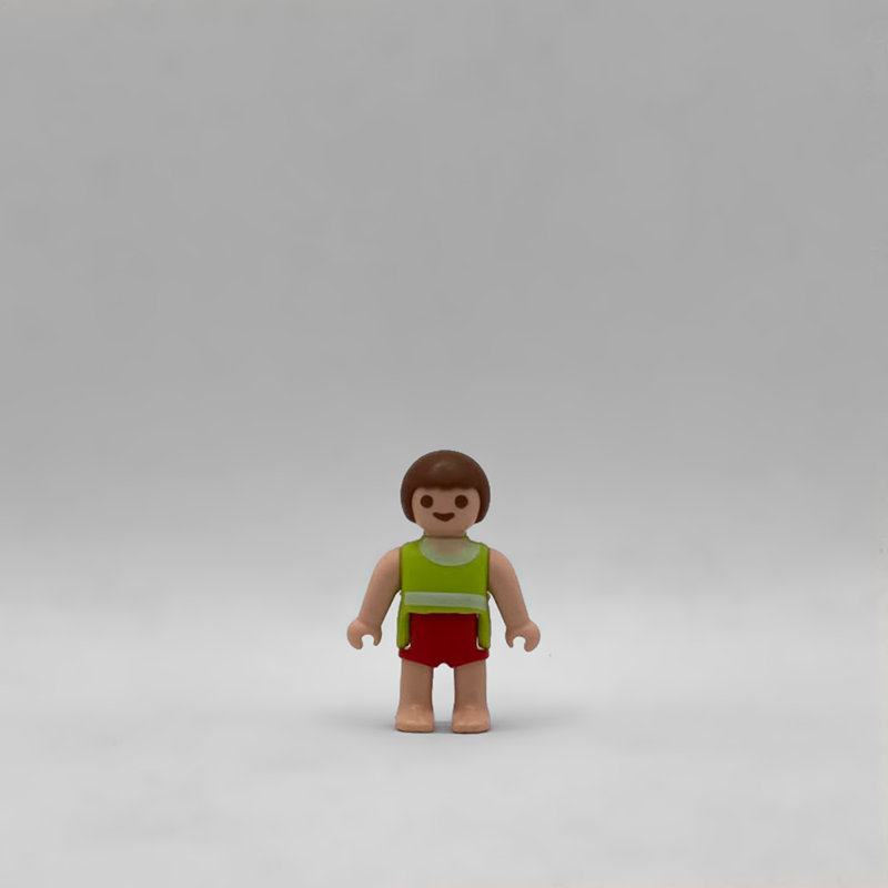 Figura Playmobil de bebé moreno con torso verde lima, franja blanca, pantalón corto rojo y pies descalzos, referencia FIG283