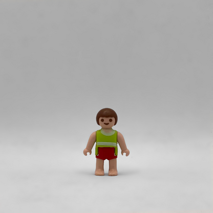 Figura Playmobil de bebé moreno con torso verde lima, franja blanca, pantalón corto rojo y pies descalzos, referencia FIG283