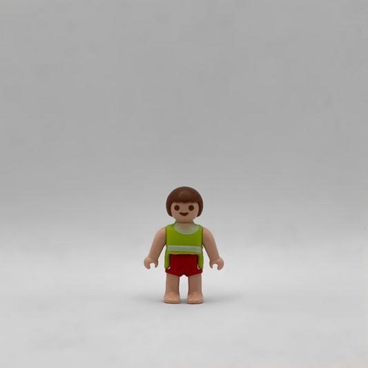 Figura Playmobil de bebé moreno con torso verde lima, franja blanca, pantalón corto rojo y pies descalzos, referencia FIG283