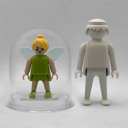 Comparativa de tamaño: Campanilla FCO1005 dentro de su urna expositora junto a una figura Playmobil estándar blanca, que no está incluida
