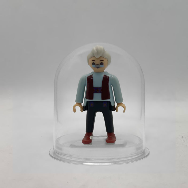 Minifigura Playmobil de Geppetto con gafas pintadas, pelo blanco y chaleco granate, sobre su peana original Playmobil dentro de la urna expositora transparente, colección Disney Kinder FCO1007