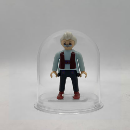 Minifigura Playmobil de Geppetto con gafas pintadas, pelo blanco y chaleco granate, sobre su peana original Playmobil dentro de la urna expositora transparente, colección Disney Kinder FCO1007