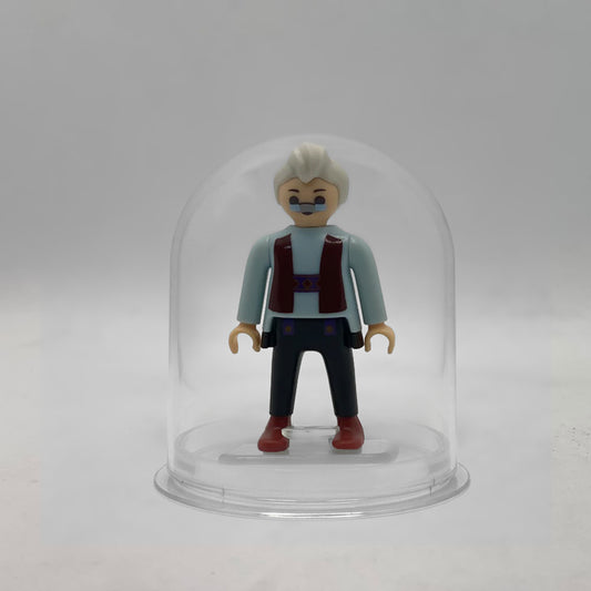 Minifigura Playmobil de Geppetto con gafas pintadas, pelo blanco y chaleco granate, sobre su peana original Playmobil dentro de la urna expositora transparente, colección Disney Kinder FCO1007