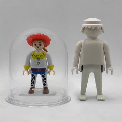 Comparativa de tamaño: Jessie FCO1008 dentro de su urna expositora junto a una figura Playmobil estándar blanca, que no está incluida