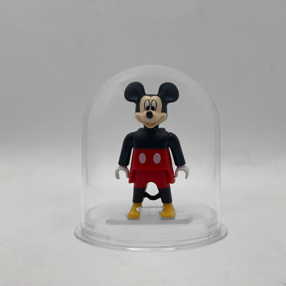 Minifigura Playmobil de Mickey Mouse con cabeza de molde exclusivo, pantalón rojo y zapatones amarillos, sobre su peana original Playmobil dentro de la urna expositora transparente, colección Disney Kinder FCO1009