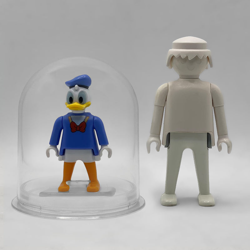 Comparativa de tamaño: el Pato Donald FCO1010 dentro de su urna expositora junto a una figura Playmobil estándar blanca, que no está incluida