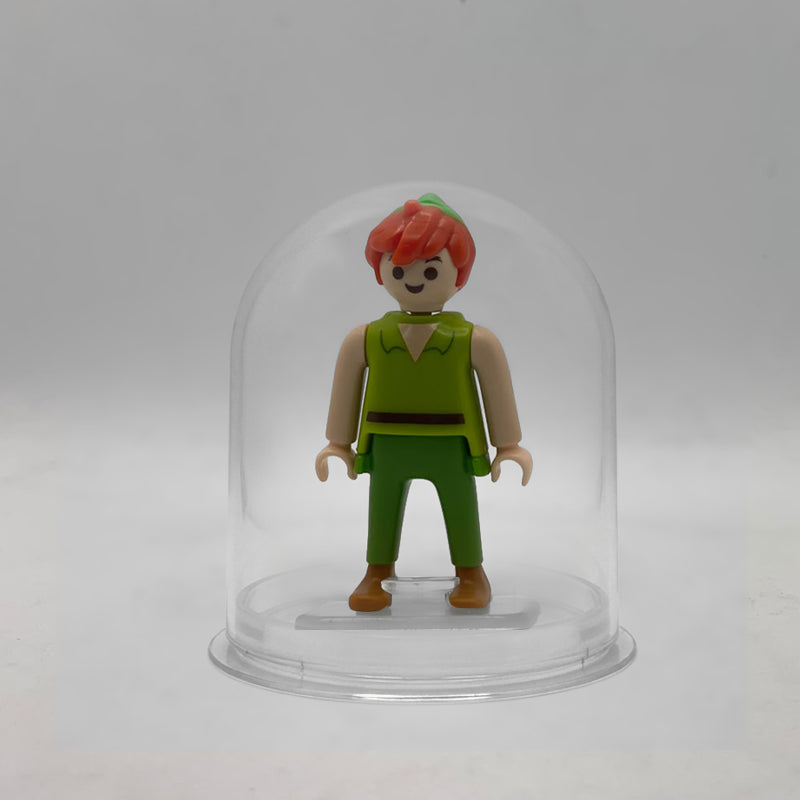 Minifigura Playmobil de Peter Pan con túnica verde, pelo pelirrojo y gorro de pico, sobre su peana original Playmobil dentro de la urna expositora transparente, colección Disney Kinder FCO1011