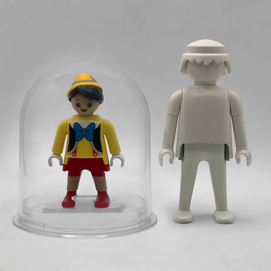 Comparativa de tamaño: Pinocho FCO1012 dentro de su urna expositora junto a una figura Playmobil estándar blanca, que no está incluida